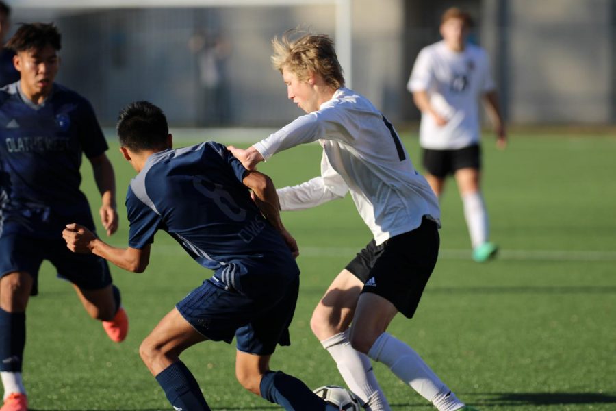 Fighting with a member of the Olathe West squad, sophomore Cooper Forcellini uses his strength to get the ball.