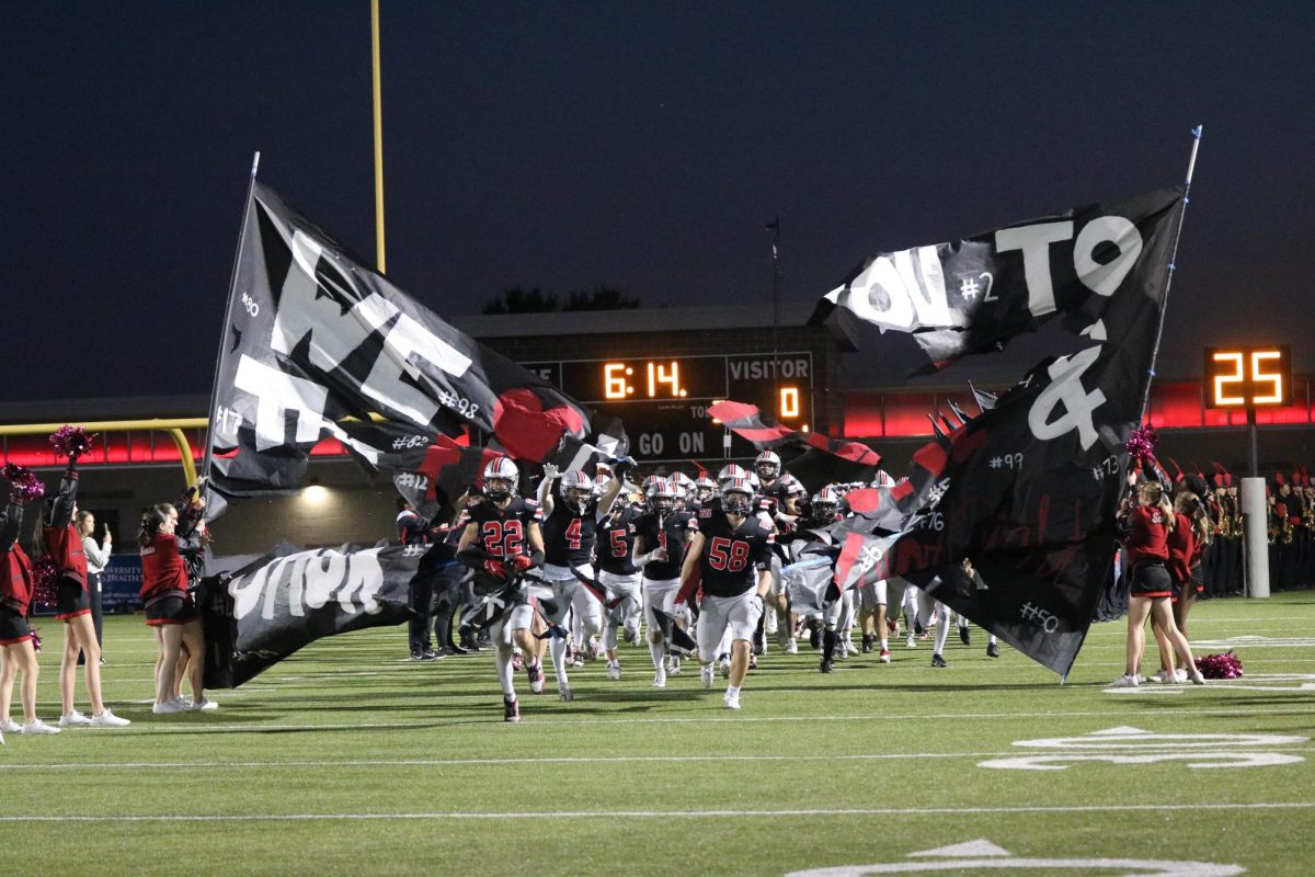 The football team runs through the banner to kick off the game.